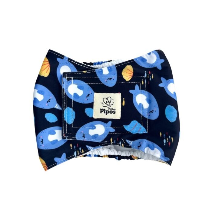 Vista frontal del pañal reutilizable para perro macho, modelo Mundo Marino Negro, con estampado de narvales azules, conchas marinas y cardúmenes de peces sobre fondo oscuro