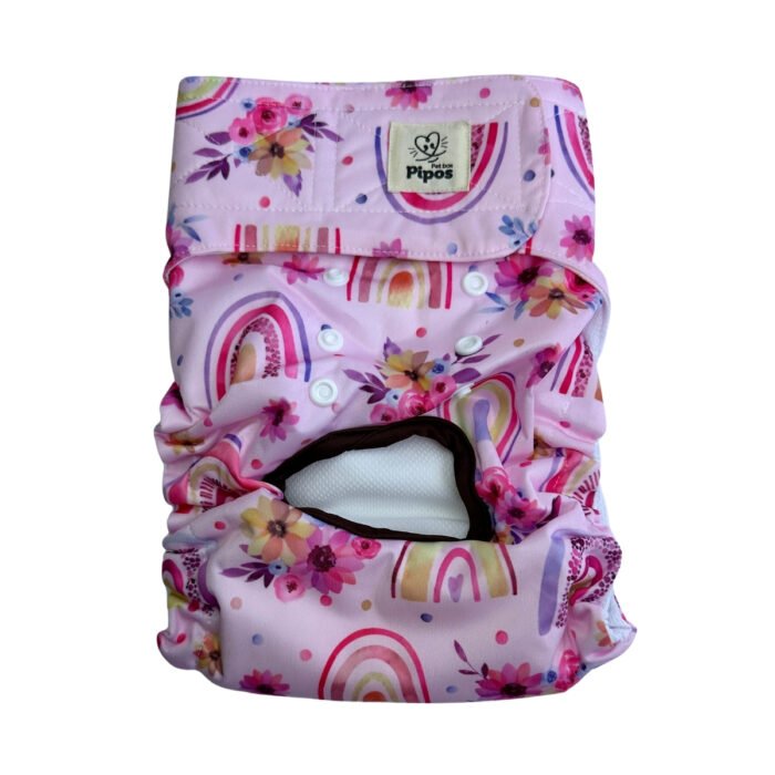 Vista frontal del pañal reutilizable para perrita, modelo Sueños Pastel, con estampado de arcoíris en tonos rosados y violetas, acompañado de flores delicadas sobre fondo rosa pastel